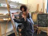 One girl painting, one girl smiling in the camera